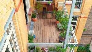 urban-farming-lahan-sempit-teras-rooftop Rak vertikal berisi tanaman sayuran hijau segar dan pot tabulampot di balkon rumah perkotaan yang disinari matahari.